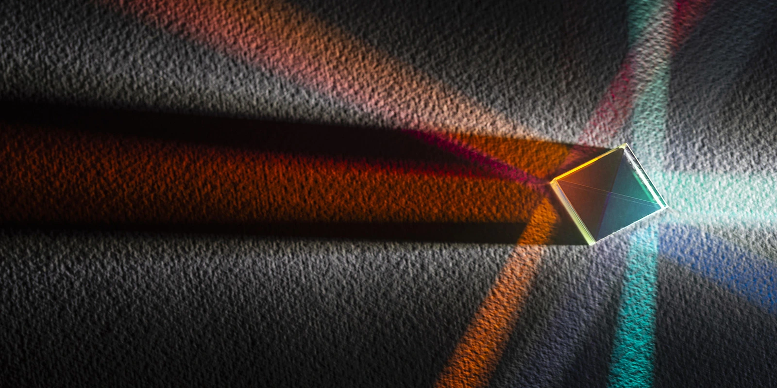 A glass prism on a dark surface, resolving a single beam of light into separate coloured channels